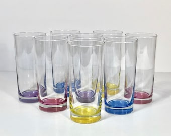 Pode incluir: Conjunto de oito copos de vidro transparente para beber com bordas coloridas. As bordas são roxas, vermelhas, amarelas e azuis.
