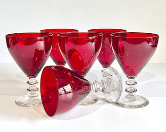 May include: Set of six red wine glasses with clear glass stems and bases. The glasses are arranged in a group, with one glass lying on its side.