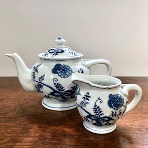 Könnte beinhalten: Ein weißes Tee-Set mit Teekanne und Milchkännchen mit einem blauen und weißen Blumenmuster. Die Teekanne hat einen Deckel und einen Ausguss. Das Milchkännchen hat einen Griff und einen Ausguss.