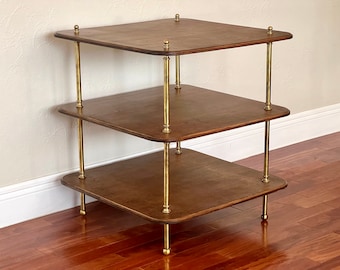 May include: A three-tiered wooden shelf unit with brass poles and rounded edges. The shelves are dark brown and the poles are polished brass.