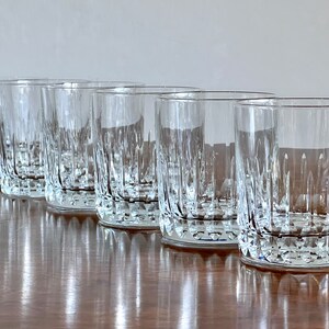 Puede incluir: Cinco vasos transparentes de vidrio con un dise&ntilde;o de vidrio cortado. Los vasos est&aacute;n dispuestos en una fila sobre una superficie de madera.