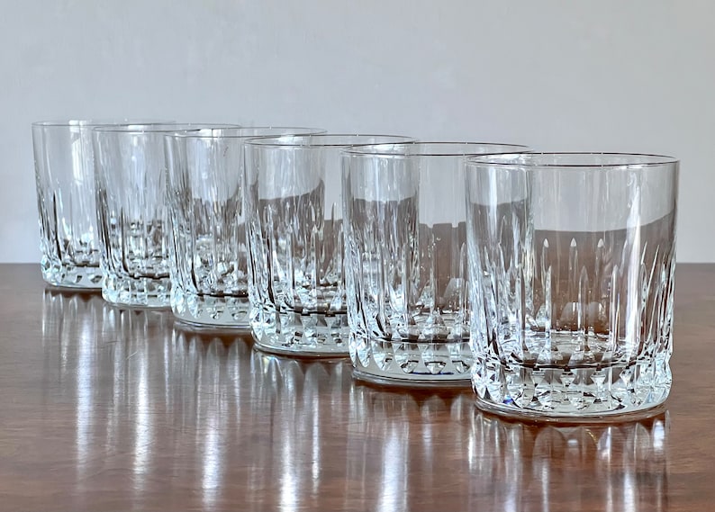 Puede incluir: Cinco vasos transparentes de vidrio con un dise&ntilde;o de vidrio cortado. Los vasos est&aacute;n dispuestos en una fila sobre una superficie de madera.