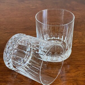 Puede incluir: Dos vasos transparentes de vidrio con un dise&ntilde;o de vidrio cortado. Los vasos est&aacute;n vac&iacute;os y se encuentran sobre una superficie de madera.