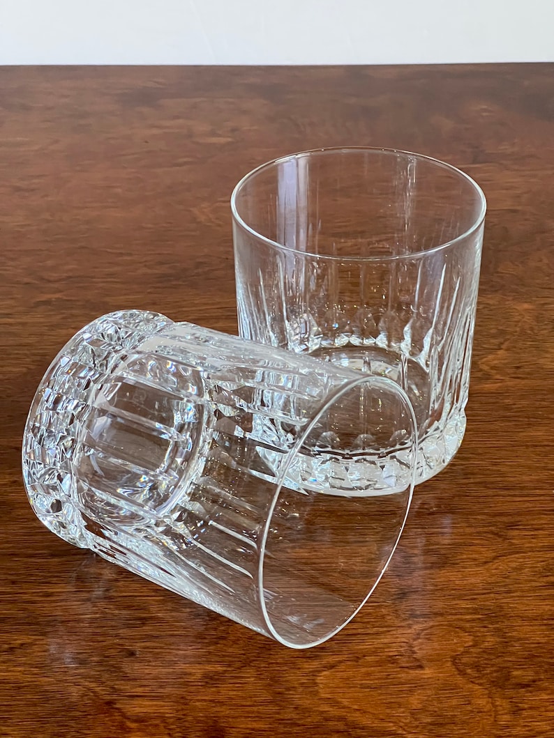 Puede incluir: Dos vasos transparentes de vidrio con un dise&ntilde;o de vidrio cortado. Los vasos est&aacute;n vac&iacute;os y se encuentran sobre una superficie de madera.