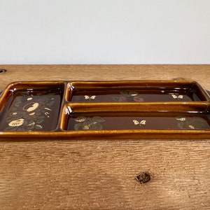 Pode incluir: Uma bandeja de servir de cerâmica marrom com três seções divididas. A bandeja tem um design floral com borboletas douradas.