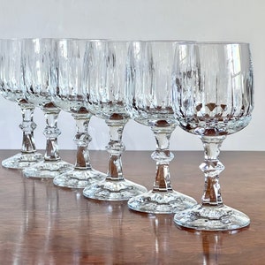 May include: Set of six clear glass wine glasses with a vertical ribbed pattern. The glasses have a tall, slender stem and a wide, round bowl.