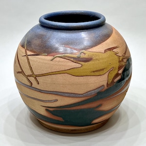May include: A round ceramic vase with a wide opening and a blue rim. The vase features a tan base with abstract designs in yellow, green, and brown. The vase is approximately 8 inches in diameter.
