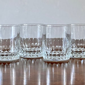 Puede incluir: Cuatro vasos transparentes de vidrio con un patr&oacute;n de corte de diamante. Los vasos est&aacute;n dispuestos en una fila sobre una superficie de madera.