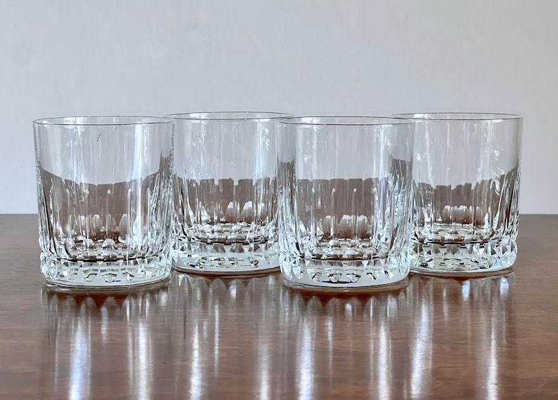 Puede incluir: Cuatro vasos transparentes de vidrio con un patr&oacute;n de corte de diamante. Los vasos est&aacute;n dispuestos en una fila sobre una superficie de madera.