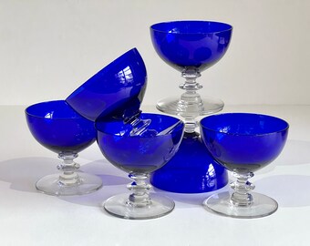 May include: Five cobalt blue glass dessert cups with clear glass stems and bases. The cups are stacked and arranged in a pyramid shape.