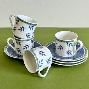May include: Set of four white porcelain coffee cups with blue and green leaf designs. Each cup is paired with a matching saucer with a blue and green border.