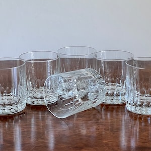 Puede incluir: Seis vasos transparentes de vidrio con un dise&ntilde;o texturizado y acanalado. Los vasos est&aacute;n dispuestos en semic&iacute;rculo sobre una superficie de madera.