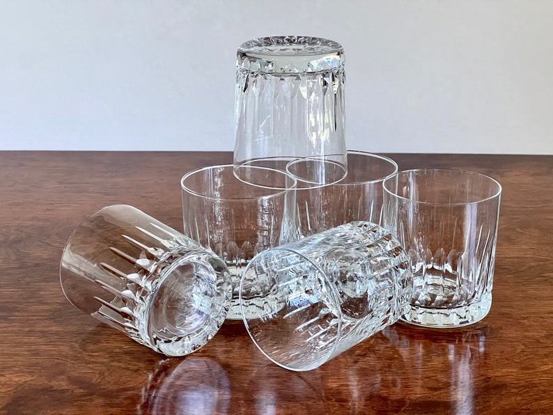 Puede incluir: Seis vasos transparentes de vidrio con un dise&ntilde;o de vidrio cortado. Los vasos est&aacute;n dispuestos en forma de pir&aacute;mide sobre una superficie de madera.