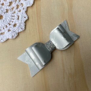 May include: A silver bow with a glitter centre and a subtle floral pattern. The bow is made of faux leather and is perfect for adding a touch of sparkle to any outfit.