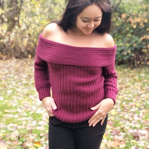 May include: A maroon off-the-shoulder sweater with long sleeves. The sweater is knitted in a ribbed pattern.