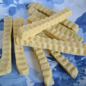 K&ouml;nnte beinhalten: Nahaufnahme eines Tellers mit hellbraunen, gewellten, knusprigen, frittierten Snacks. Die Snacks sind auf einem wei&szlig;en Teller mit blauem Blumendesign gestapelt.