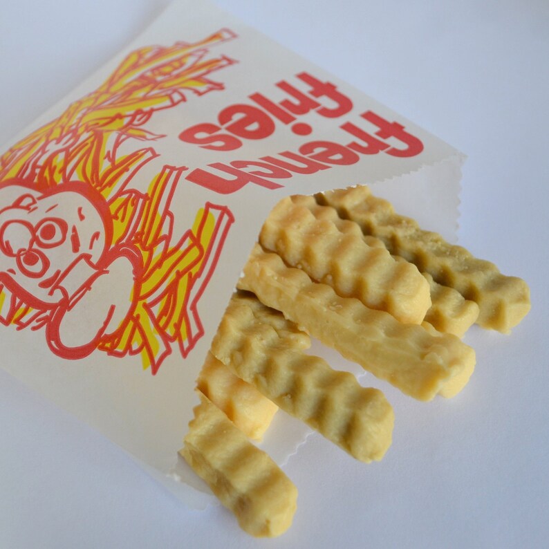 K&ouml;nnte beinhalten: Ein wei&szlig;er Papierbeutel mit der Aufschrift "French Fries" in Rot. Der Beutel ist teilweise ge&ouml;ffnet und zeigt einen Haufen goldbrauner, knuspriger Pommes Frites.