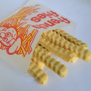 K&ouml;nnte beinhalten: Ein wei&szlig;er Papierbeutel mit der Aufschrift "French Fries". Der Beutel ist offen und mit mehreren goldbraunen, gewellten Pommes Frites gef&uuml;llt.