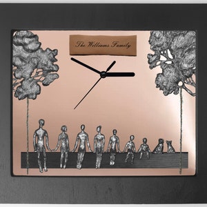 May include: A copper-colored clock with a black frame and a silver-colored design of a family sitting on a bench under two trees. The clock face is white with black hands. The text "The Williams Family" is on a brown tag above the clock face.
