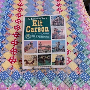 May include: The Golden Stamp Book of Kit Carson, a vintage activity book featuring a dark green cover with yellow text and multiple illustrated panels depicting historical scenes of the Old West, including scouts and frontiersmen, with a 50 cent price tag.