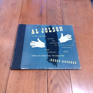 May include: Vintage vinyl record album cover for Al Jolson, featuring the text "Al Jolson in songs he made famous." The cover is blue with white hand illustrations and song titles. The record is from Decca Records.
