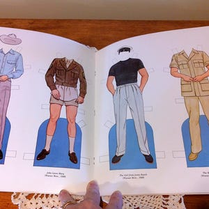 May include: Open book with vintage paper dolls. Four figures are depicted wearing different outfits, including a blue shirt and pink pants, a brown jacket and shorts, a black shirt and light blue pants, and a tan uniform. The text includes the names of the characters and the year.