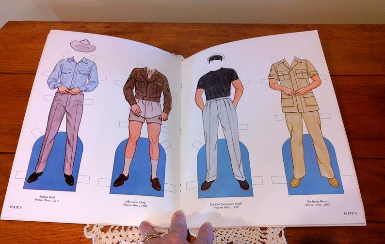 May include: Open book with vintage paper dolls. Four figures are depicted wearing different outfits, including a blue shirt and pink pants, a brown jacket and shorts, a black shirt and light blue pants, and a tan uniform. The text includes the names of the characters and the year.