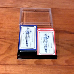May include: Two decks of playing cards, one with a blue border and the other with a red border, are displayed on a black stand. Each card features a blue and white architectural illustration. A clear plastic case sits above the cards.