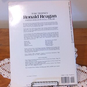 May include: The back cover of a paperback book titled "Ronald Reagan Paper Dolls in Full Color" by Tom Tierney. The book features a biography and paper doll illustrations. The book measures 9.25 x 12 inches.
