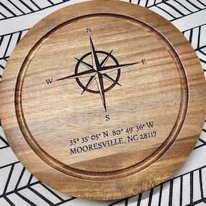 May include: A round wooden cutting board with a compass design and the coordinates 35° 35' 05" N 80° 49' 36" W and the text "MOORESVILLE, NC 28117".