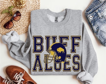 May include: Gray sweatshirt with the text "BUFF ALOES" in navy blue with a gold outline. A navy blue football helmet with a gold buffalo logo is centered between the words.