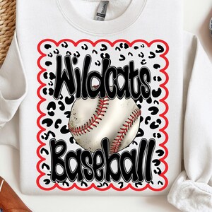 Peut inclure: Sweat-shirt blanc avec un motif graphique rouge, blanc et noir. Le graphique représente un ballon de baseball, les mots "Wildcats Baseball" et un motif léopard.