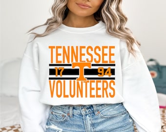 May include: White sweatshirt featuring the word "TENNESSEE" in orange block letters. Below is a black and orange striped design with the numbers "17" and "94". The word "VOLUNTEERS" is printed below the numbers in orange.