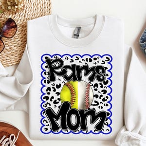 Könnte beinhalten: Weißer Pullover mit einem blauen und schwarzen Grafikdesign. Die Grafik zeigt einen Softball, Leopardenmuster und den Text "Rams Mom".