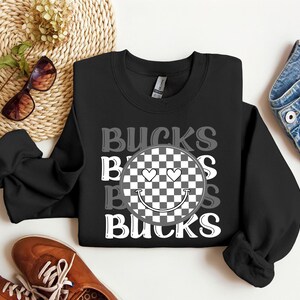 May include: Black sweatshirt with a checkered smiley face and the text "Bucks" repeated in a vertical pattern.