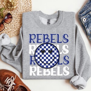May include: A gray sweatshirt with the words "Rebels" in blue and white, with a checkered smiley face in between. The smiley face has hearts for eyes.