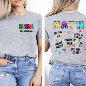 May include: Gray t-shirt with a math-themed design. The front of the shirt says "PEMDAS" with the order of operations symbols and "MRS. CRAWFORD". The back of the shirt says "MATH" in colorful letters and includes math equations, symbols, and phrases like "Rise Over Run", "Show Your Work", and "You Can Do It!"