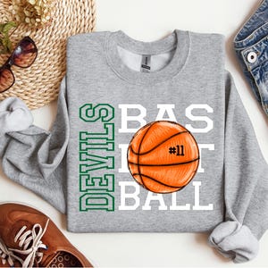 May include: Gray sweatshirt with the words "Devils Basketball" in green and white lettering. A basketball with the number "#11" is in the center of the design.