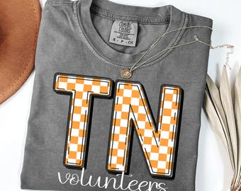 May include: A gray t-shirt with a checkered orange and white "TN" graphic and the text "volunteers" underneath.