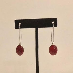 Può includere: Un paio di orecchini a cerchio d'argento con un ciondolo di pietra rossa. Gli orecchini sono appesi a un espositore nero.