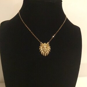 May include: A gold chain necklace with a lion head pendant. The pendant is covered in sparkling rhinestones.