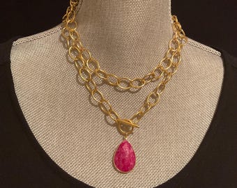 Pode incluir: Um colar de corrente de ouro com um pingente de gota rosa. O colar é composto por duas correntes de tamanhos diferentes.