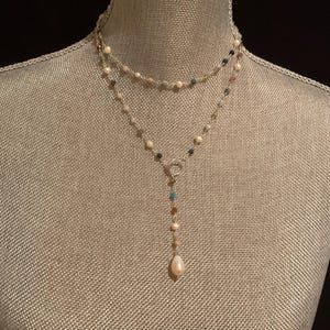 May include: A two-strand necklace with a silver chain and a variety of small, colorful beads. The necklace has a Y-shaped pendant with a single, teardrop-shaped pearl at the end. The necklace is displayed on a mannequin.
