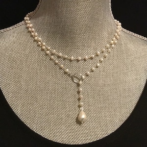 May include: A delicate pearl necklace with a single large pearl pendant. The necklace is made of small, white pearls and is layered for a classic look.