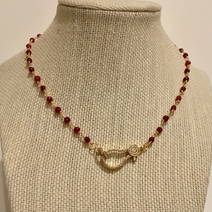 May include: A gold chain necklace with red beads and a gold clasp with clear stones.