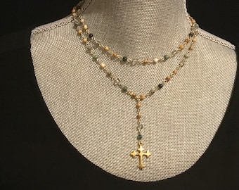 Puede incluir: Un collar de varios niveles con un colgante de cruz dorada. El collar está hecho de pequeñas cuentas multicolores, incluyendo verde, marrón y blanco.