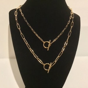 May include: Two gold chain necklaces with toggle clasps. The chains are layered on a black mannequin.