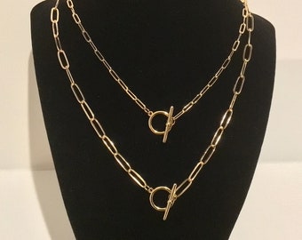 May include: Two gold chain necklaces with toggle clasps. The chains are layered on a black mannequin.