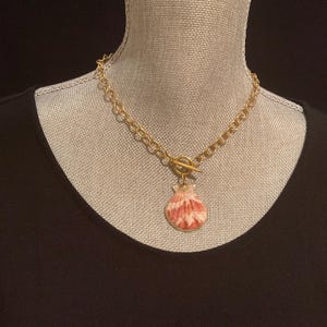 May include: A gold chain necklace with a toggle clasp and a pink and white seashell pendant.