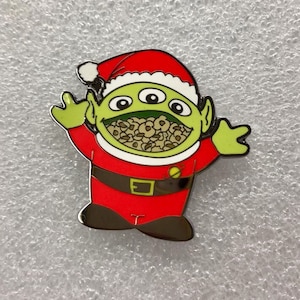 May include: A green alien wearing a red Santa suit with a white trim and a white Santa hat. The alien has three eyes and is holding its arms out. The alien's mouth is open and filled with brown cereal.